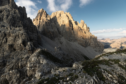 View of the jagged peaks of the Dolomites with sunlight illuminating the rocky cliffs under a blue sky in Trentino Alto Adige Italy. View of the jagged peaks of the Dolomites with sunlight illuminating the rocky cliffs under a blue sky in Trentino Alto Adige Italy.