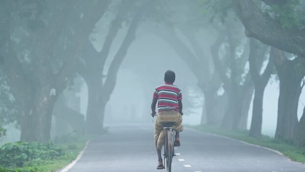 View of a man cycling on a foggy road in Bogura Bangladesh.