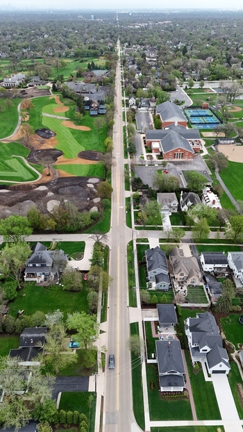 Aerial view of a long straight road with a car stretching through a residential neighborhood with a golf course and lush green trees Indianapolis. Aerial view of a long straight road with a car stretching through a residential neighborhood with a golf course and lush green trees Indianapolis.