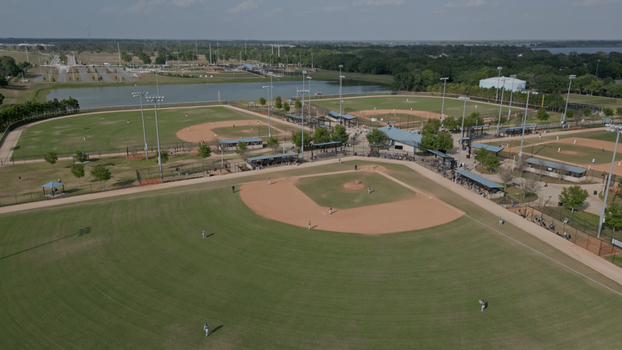 Aerial view of a baseball field complex with multiple diamonds manicured grass dirt infields and players practicing under a clear sky in Polk City Florida United States. Aerial view of a baseball field complex with multiple diamonds manicured grass dirt infields and players practicing under a clear sky in Polk City Florida United States.