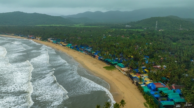 Aerial view of Palolem Beach with its sandy coastline dense palm trees colorful beach huts and rolling hills under a cloudy sky in Canacona Goa India.