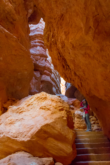 View of Bryce Canyon National Park with a woman standing on stone stairs between towering orange rock walls in Utah United States.