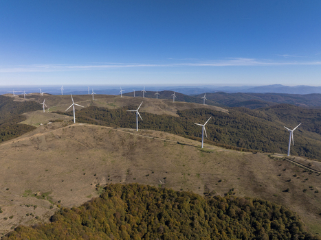 Aerial view of wind turbines situated on rolling hills covered with autumn forests under a clear blue sky in Bulgaria. Aerial view of wind turbines situated on rolling hills covered with autumn forests under a clear blue sky in Bulgaria.