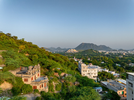 Aerial view of traditional hillside architecture surrounded by lush greenery with the urban landscape of Udaipur in the background Udaipur Rajasthan India.