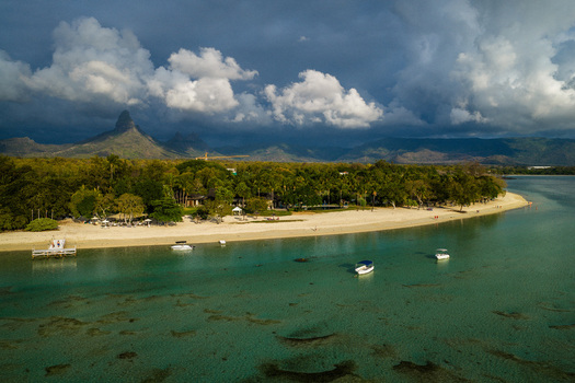 Aerial view of a tropical beach on Mauritius Island with white sand turquoise water anchored boats and a wooden pier against lush greenery in Moka District Mauritius. Aerial view of a tropical beach on Mauritius Island with white sand turquoise water anchored boats and a wooden pier against lush greenery in Moka District Mauritius.