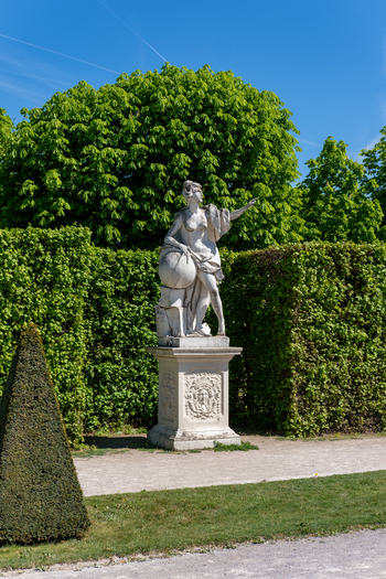 View of a white marble statue with a globe in the gardens of Belvedere Palace surrounded by manicured green hedges and lush trees in Vienna Austria. View of a white marble statue with a globe in the gardens of Belvedere Palace surrounded by manicured green hedges and lush trees in Vienna Austria.