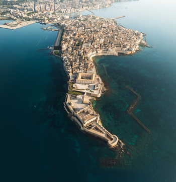 Aerial view of the historic Island of Ortigia featuring Castello Maniace surrounded by the turquoise waters of the Ionian Sea in Syracuse Sicily Italy.