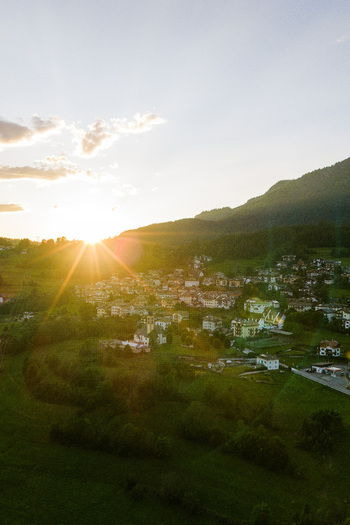 Aerial view of Val di Fiemme at sunset with a small village nestled in the valley surrounded by lush green meadows and rolling mountains under a golden sky Trentino Alto Adige Italy.
