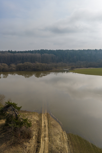 Aerial view of a flooded landscape with a dirt road submerged in water surrounded by dense forest and green fields under an overcast sky Kaniukai Kaunas County Lithuania. Aerial view of a flooded landscape with a dirt road submerged in water surrounded by dense forest and green fields under an overcast sky Kaniukai Kaunas County Lithuania.