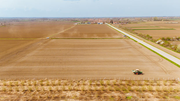 Aerial view of a tractor tilling the pale earth of vast geometric fields under a soft sky contrasting with the green of the roadside Sremska Mitrovica Vojvodina Serbia. Aerial view of a tractor tilling the pale earth of vast geometric fields under a soft sky contrasting with the green of the roadside Sremska Mitrovica Vojvodina Serbia.