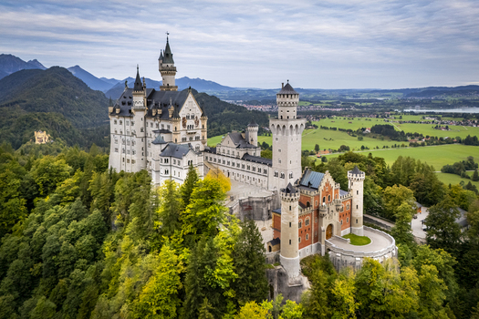 Aerial view of Neuschwanstein Castle a fairy tale fortress perched atop a verdant hill its spires piercing the sky above the Bavarian landscape Füssen Bayern Germany. Aerial view of Neuschwanstein Castle a fairy tale fortress perched atop a verdant hill its spires piercing the sky above the Bavarian landscape Füssen Bayern Germany.