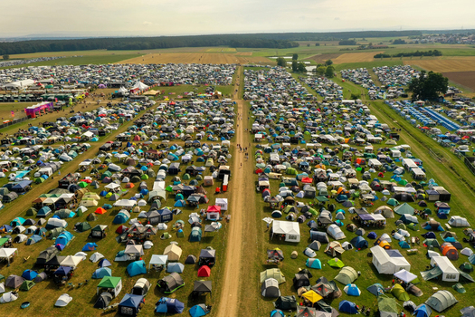 Aerial view of the Open Beatz Festival campsite featuring thousands of colorful tents on green fields divided by a central path near a forest Herzogenaurach Bayern Germany.