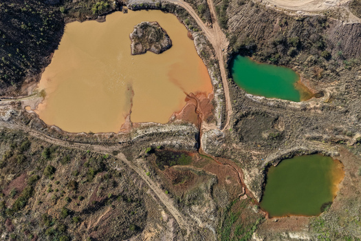 Aerial view of industrial waste ponds from mining operations showing discoloured water in shades of green brown and orange surrounded by barren landscape in Welkom Free State South Africa.