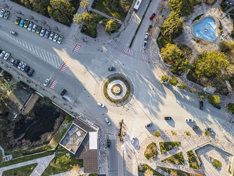 Aerial view of Sheshi Pavaresia featuring a central roundabout surrounding streets with parked cars a blue fountain and urban greenery in Fier Qarku i Fierit Albania. Aerial view of Sheshi Pavaresia featuring a central roundabout surrounding streets with parked cars a blue fountain and urban greenery in Fier Qarku i Fierit Albania.