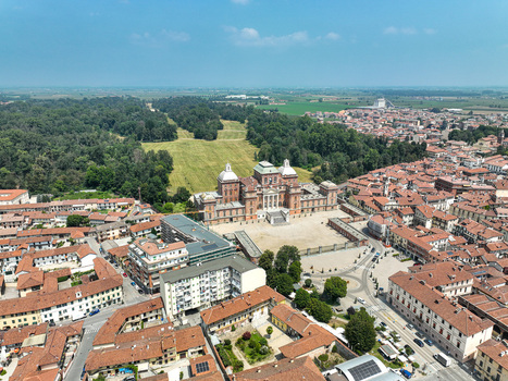 Aerial view of the Royal Palace of Racconigi with its grand facade and courtyard surrounded by red tiled rooftops and a lush green park under a clear sky in Racconigi Piemonte Italy.