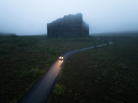 Aerial view of a car driving on a road towards the massive rock formation of Asbyrgi canyon surrounded by misty landscape Nordurthing Iceland.