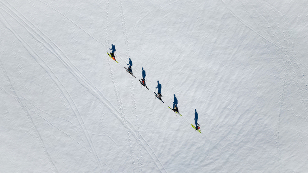 Aerial view of a group of skiers trekking in a line across a pristine snow covered mountain slope with long shadows Le Reposoir Auvergne Rhone Alpes France. Aerial view of a group of skiers trekking in a line across a pristine snow covered mountain slope with long shadows Le Reposoir Auvergne Rhone Alpes France.