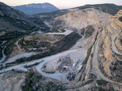 Aerial view of an open pit stone quarry with terraced rock faces heavy machinery processing equipment and winding access roads in Teulada Valencian Community Spain.