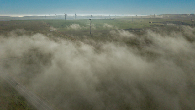 Aerial view of a wind farm with numerous turbines rising above low lying clouds and mist covering the green fields and a road in Vredenburg Western Cape South Africa. Aerial view of a wind farm with numerous turbines rising above low lying clouds and mist covering the green fields and a road in Vredenburg Western Cape South Africa.