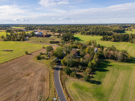 Aerial view of the Swedish countryside in Rimbo featuring a winding road through fields forest patches and red farm buildings under a clear sky in Stockholm County Sweden.