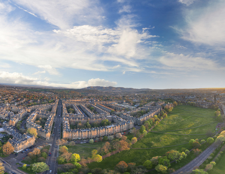 Aerial view of historic stone residential terraces and a lush green park under a soft blue sky with wispy clouds in Edinburgh Scotland United Kingdom. Aerial view of historic stone residential terraces and a lush green park under a soft blue sky with wispy clouds in Edinburgh Scotland United Kingdom.