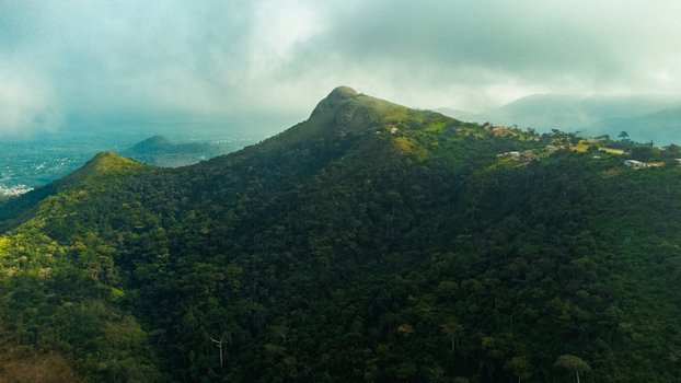 Aerial view of Mt. Gemi surrounded by lush green forested slopes rolling hills and misty clouds under a soft sky in Amedzofe Volta Region Ghana. Aerial view of Mt. Gemi surrounded by lush green forested slopes rolling hills and misty clouds under a soft sky in Amedzofe Volta Region Ghana.