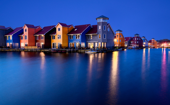 View of colorful houses along the Reitdiephaven canal at twilight with reflections on the water surface in the Netherlands. View of colorful houses along the Reitdiephaven canal at twilight with reflections on the water surface in the Netherlands.