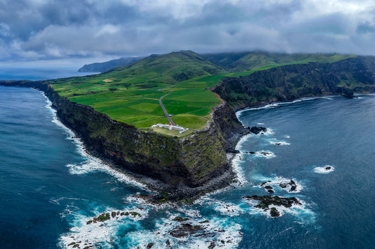 Aerial view of the lighthouse standing guard where the green land dramatically meets the restless Atlantic ocean Flores A&ccedil;ores Portugal.