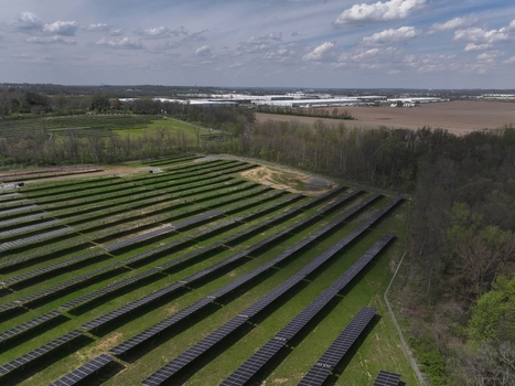 Lebanon United States 12 April 2026 Aerial view of a solar farm with rows of photovoltaic panels surrounded by green fields and dense forest under a cloudy sky.
