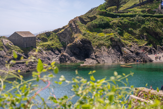 View of a stone building perched on a rocky cliff overlooking the clear green waters of the tidal pool in the coastal village of Polperro Cornwall United Kingdom. View of a stone building perched on a rocky cliff overlooking the clear green waters of the tidal pool in the coastal village of Polperro Cornwall United Kingdom.