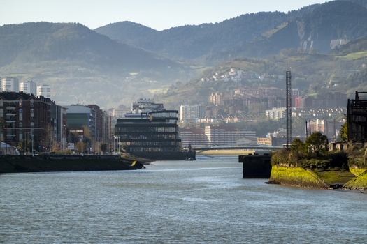 View of the Nervion river flowing through the urban landscape with modern architecture and lush green mountains in the background Greater Bilbao Basque Country Spain. View of the Nervion river flowing through the urban landscape with modern architecture and lush green mountains in the background Greater Bilbao Basque Country Spain.