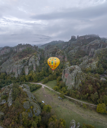 Aerial view of a colorful hot air balloon floating above the unique sandstone rock formations of the Belogradchik Rocks surrounded by autumn forest in Belogradchik Vidin Bulgaria.