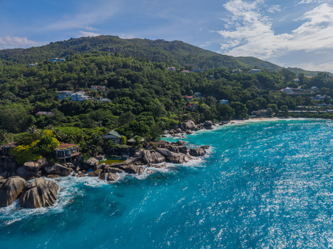 Aerial view of azure waves crash against the rocky shore beneath lush green hillsides La Retraite Mahe Island Seychelles. Aerial view of azure waves crash against the rocky shore beneath lush green hillsides La Retraite Mahe Island Seychelles.