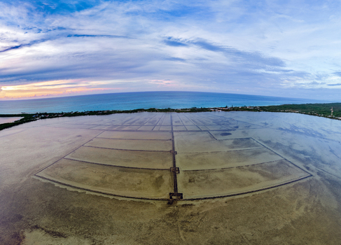 Aerial view of the Salt Pond evaporation basins with geometric patterns near the turquoise coastline under a soft sunset sky in Exuma Exuma The Bahamas.
