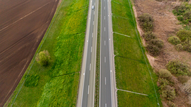 Aerial view of a stark highway slicing through vibrant green fields against the backdrop of rich dark soil Sremska Mitrovica Vojvodina Serbia. Aerial view of a stark highway slicing through vibrant green fields against the backdrop of rich dark soil Sremska Mitrovica Vojvodina Serbia.