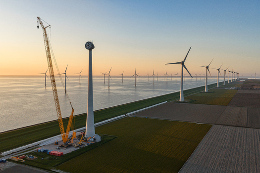 Aerial view of wind turbines under construction with a large yellow crane on a coastal field at sunset Netherlands.