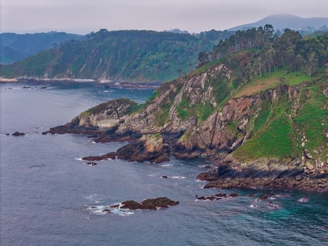 Aerial view of rugged green cliffs and rocky coastline along the Cantabrian Sea under a misty sky in Cudillero Asturias Spain. Aerial view of rugged green cliffs and rocky coastline along the Cantabrian Sea under a misty sky in Cudillero Asturias Spain.