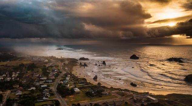 Aerial view of a dramatic winter storm over the coastline featuring dark clouds golden sunset light crashing waves and sea stacks in Bandon Oregon United States. Aerial view of a dramatic winter storm over the coastline featuring dark clouds golden sunset light crashing waves and sea stacks in Bandon Oregon United States.
