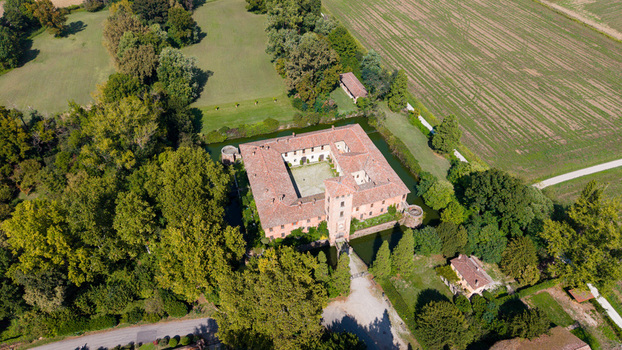 Aerial view of the historic Castello di Peschiera Borromeo surrounded by a moat lush green trees and agricultural fields in Peschiera Borromeo Lombardia Italy.