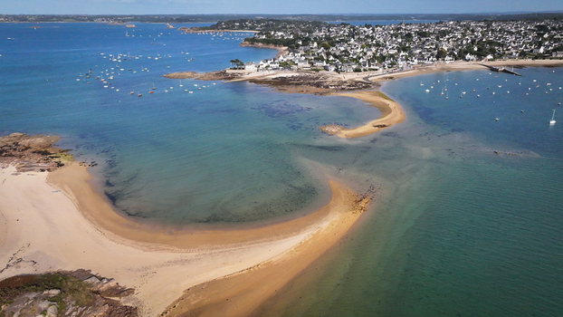 Aerial view of the vivid turquoise sea meeting the sandy beach and rocky coastline boats dotting the horizon Carantec Brittany France.