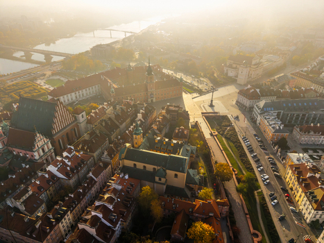 Aerial view of the historic Royal Castle and red roofed buildings of the Old Town under a hazy golden sky with the Vistula river in the background of Warsaw Poland. Aerial view of the historic Royal Castle and red roofed buildings of the Old Town under a hazy golden sky with the Vistula river in the background of Warsaw Poland.