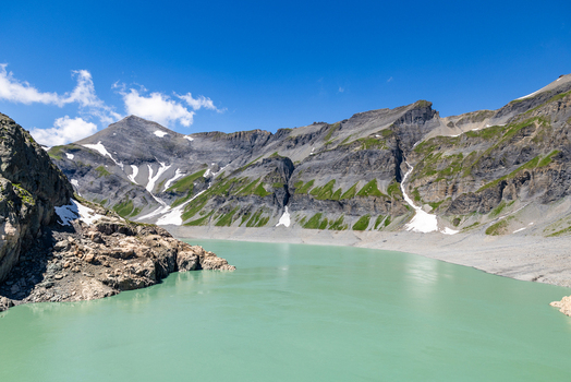 View of the turquoise waters of Emosson Lake surrounded by rugged mountain peaks with patches of snow under a clear blue sky at VerticAlp Emosson in Le Chatelard Fribourg Switzerland. View of the turquoise waters of Emosson Lake surrounded by rugged mountain peaks with patches of snow under a clear blue sky at VerticAlp Emosson in Le Chatelard Fribourg Switzerland.