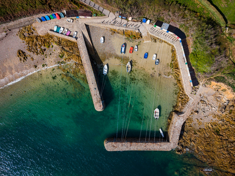 Aerial view of Port Racine a small historic stone harbor with colorful fishing boats moored in clear turquoise water surrounded by rocky coastline in La Hague Normandie France.