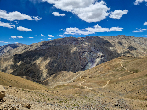 View of the winding Penzi La road traversing the arid mountainous landscape under a bright blue sky with scattered clouds in Zanskar Ladakh India.