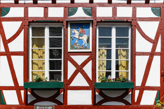 View of a traditional half timbered house facade featuring a Saint George icon red timber framing and green window boxes in Monreal Rhineland Palatinate Germany. View of a traditional half timbered house facade featuring a Saint George icon red timber framing and green window boxes in Monreal Rhineland Palatinate Germany.