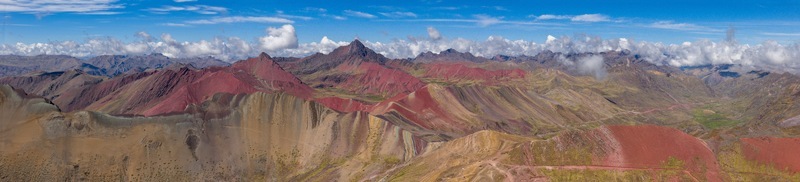 Aerial view of Vinicunca Rainbow Mountain featuring vibrant mineral rich slopes and rugged peaks under a bright blue sky with scattered clouds in the Andes Cusco Cuzco Peru. Aerial view of Vinicunca Rainbow Mountain featuring vibrant mineral rich slopes and rugged peaks under a bright blue sky with scattered clouds in the Andes Cusco Cuzco Peru.