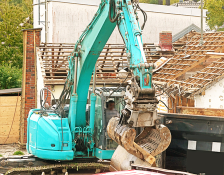 View of a teal excavator with a grapple attachment working at a building demolition site in Garching Bavaria Germany.