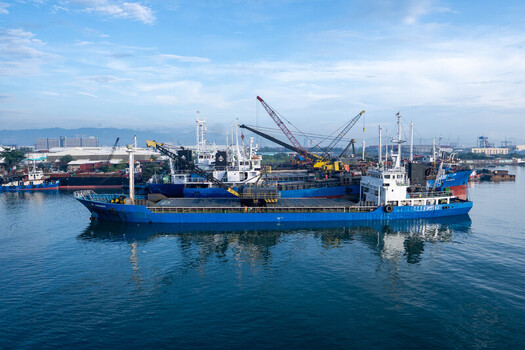 View of the Cebu Port Authority with a blue cargo ship docked in the harbor featuring industrial cranes and calm waters in Cebu City Central Visayas Philippines. View of the Cebu Port Authority with a blue cargo ship docked in the harbor featuring industrial cranes and calm waters in Cebu City Central Visayas Philippines.