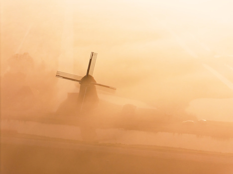 Aerial view of the historic windmill at Polder de Lage Hoek shrouded in thick morning mist during a golden sunrise Hoogwoud Noord Holland Netherlands.