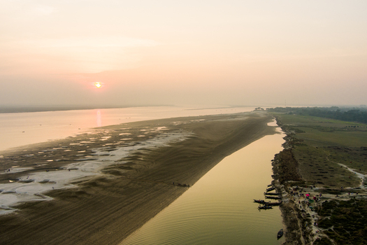 Aerial view of the Padma River at sunset with sandy banks small boats moored along the shore and people walking on the riverbank in Rajshahi Rajshahi Division Bangladesh.